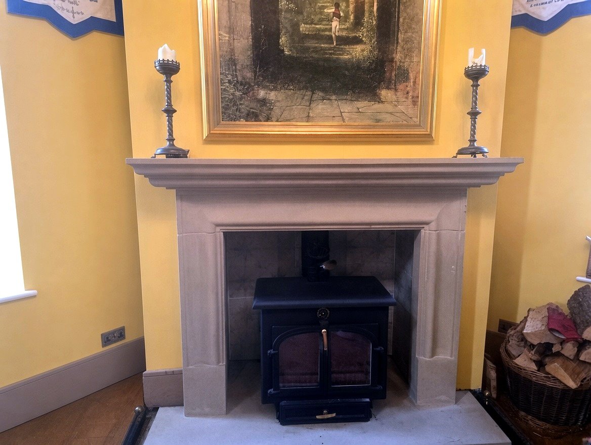 A stone fireplace surround with a wood-burning stove, made and fitted by Staves Stonemasonry